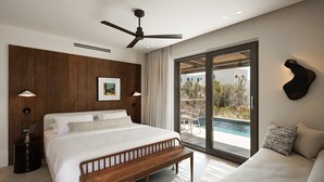 Un dormitorio moderno con una cama grande, un banco, un ventilador de techo y vistas a una piscina exterior.