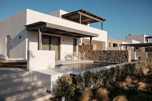 Una casa moderna con piscina, mobiliario exterior y un muro de piedra.