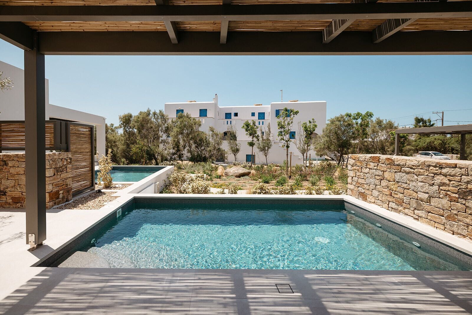 A swimming pool with a stone wall and a view of a white building with blue windows.