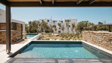A swimming pool with a stone wall and a view of a white building with blue windows.