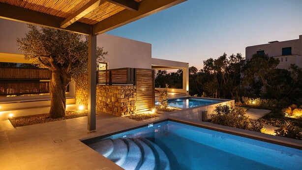 A modern outdoor pool area with stone walls and wooden pergolas, surrounded by greenery. - Omma Suites (Naxos)