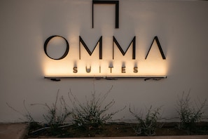Un letrero de hotel con el nombre 'OMMA SUITES' iluminado en una pared.