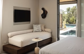 Quarto moderno com sofá-cama, mesa de cabeceira pequena, televisão na parede e vista para uma piscina.