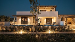 A modern two-story house with a swimming pool, outdoor seating, and a well-lit patio area. - Omma Suites (Naxos)