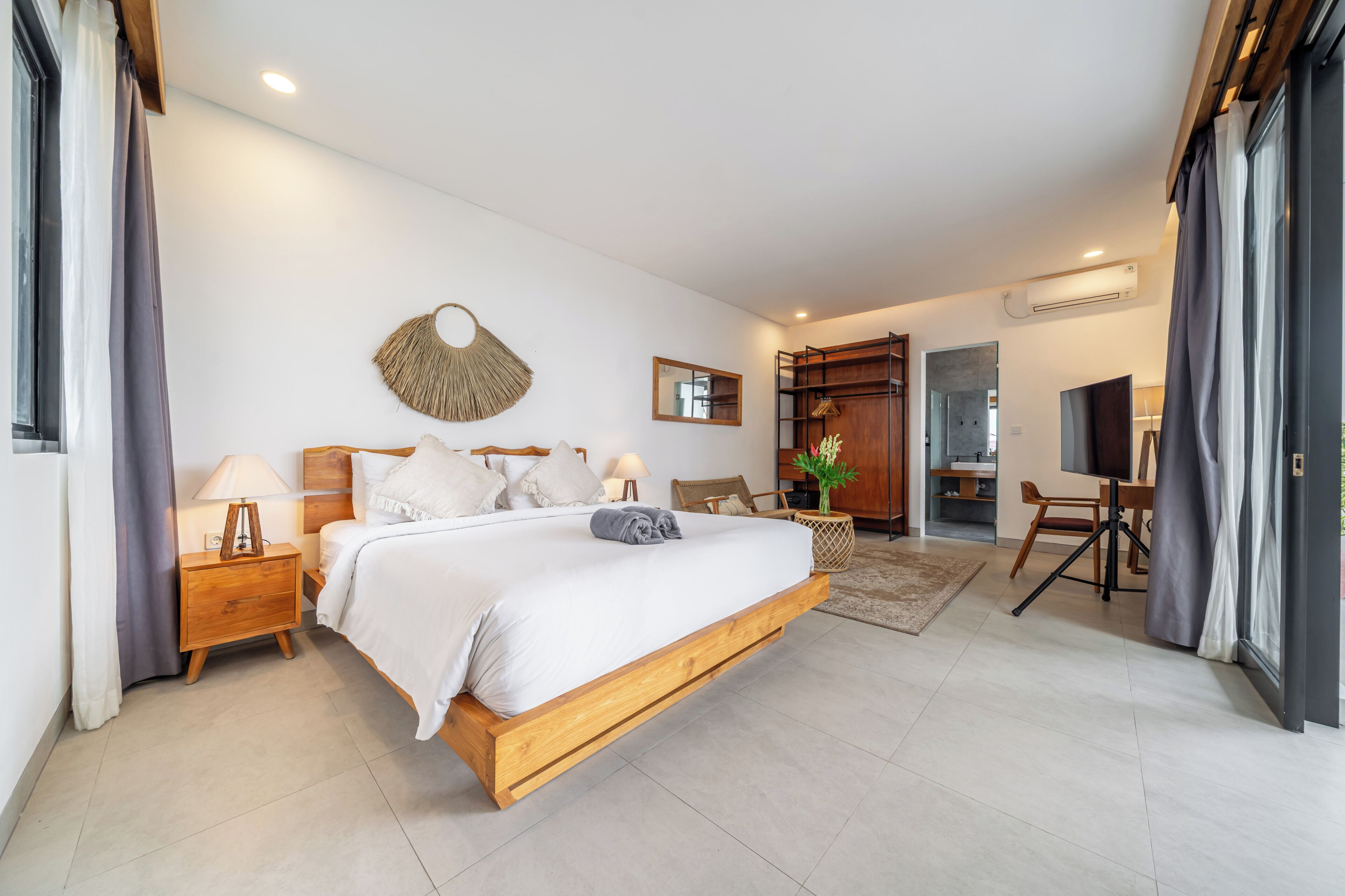 Un dormitorio con cama de madera, mesitas de noche, un espejo, un ventilador de pared y vistas al baño.