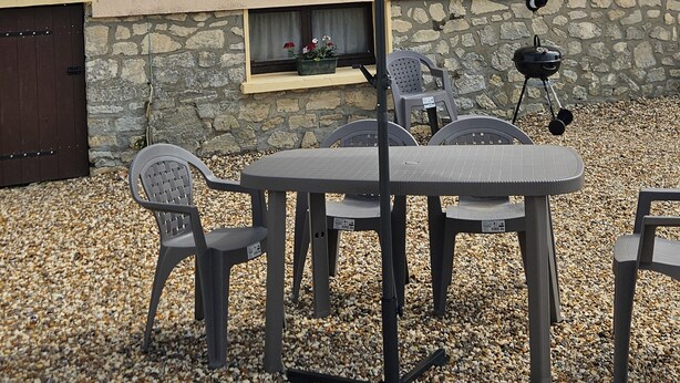 An outdoor patio with a table and chairs, a large umbrella, a grill, and a stone wall. - Little cocoon (Ferrières-en-Bray)