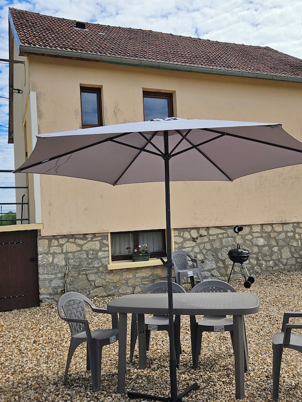 Un patio al aire libre con mesa y sillas, un paraguas grande, una parrilla y una pared de piedra.