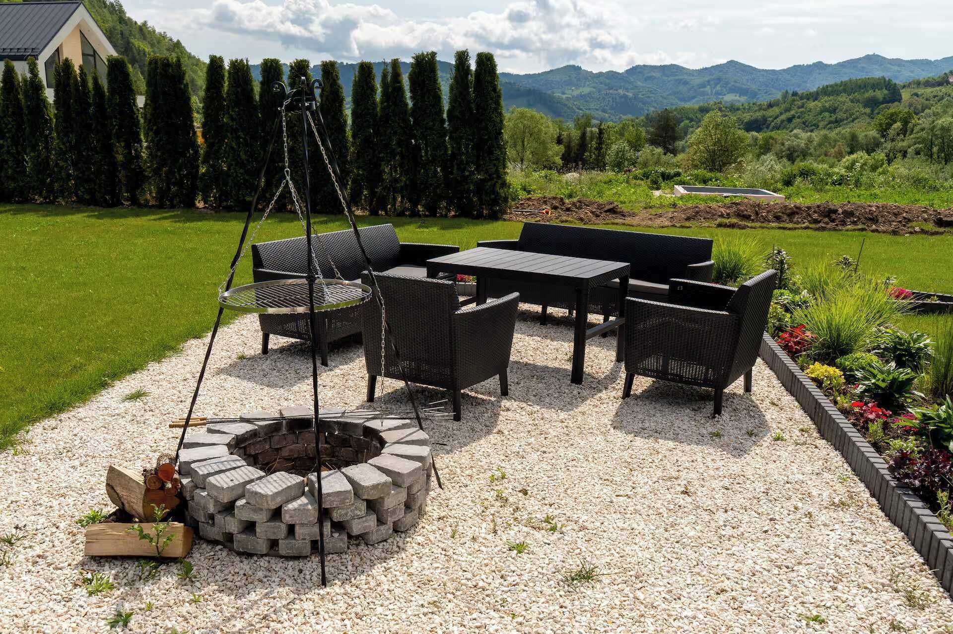 Een terras met tuinmeubilair, een vuurkuil en uitzicht op een bergachtig landschap.