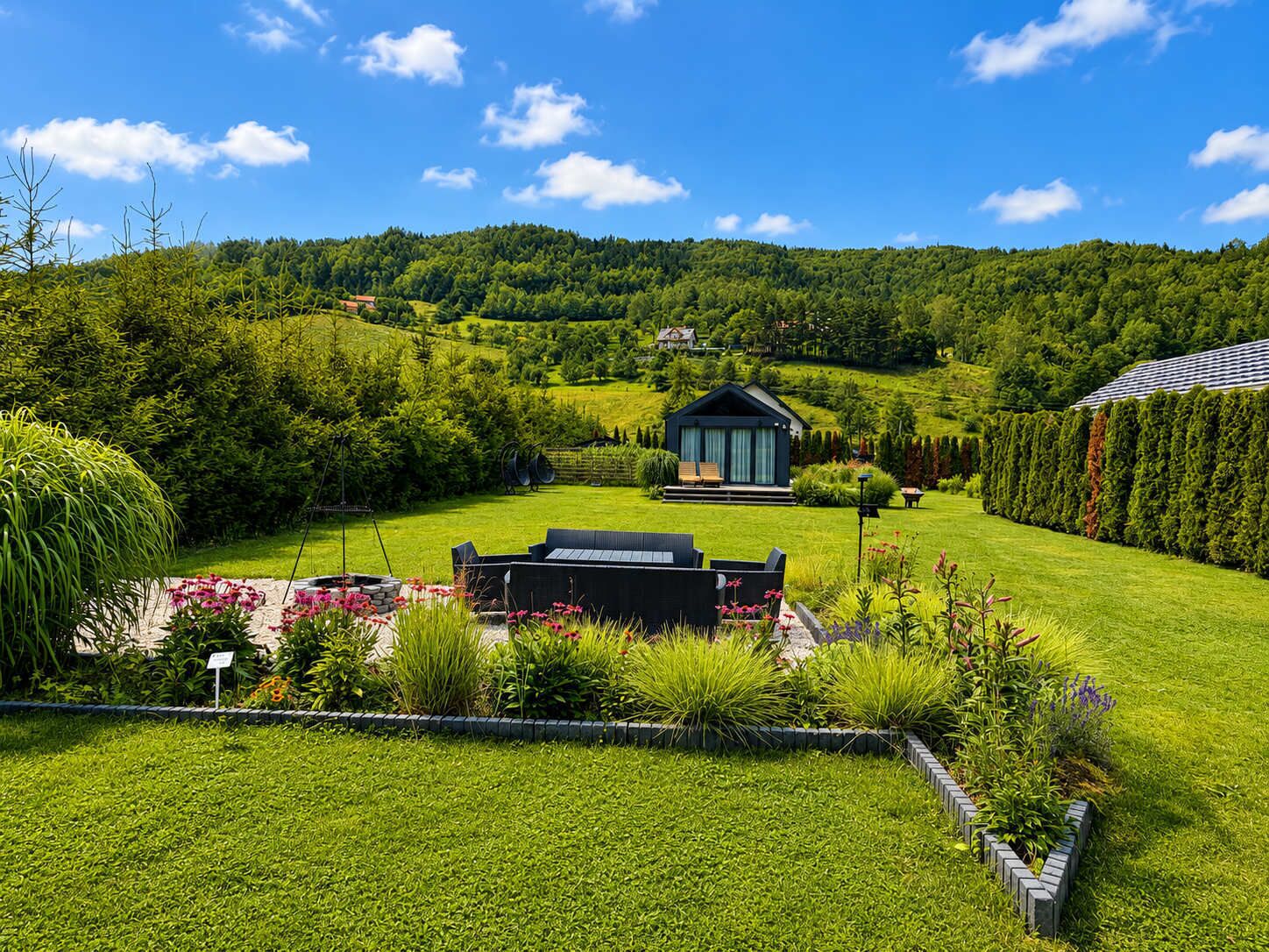 A modern house with a well-maintained garden, a small deck, and a view of the surrounding forested hills.