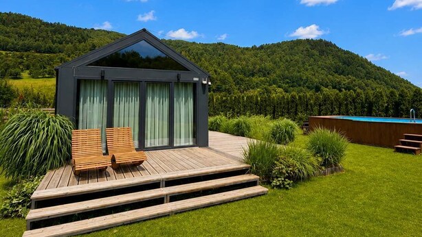 Una casa moderna con terraza, piscina y una colina boscosa al fondo.