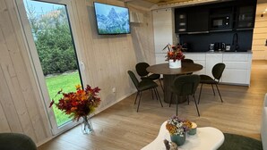 Una cocina moderna con un televisor de pantalla plana, una zona de comedor con una mesa redonda y sillas, y un gran ventanal corredero que da a un jardín.