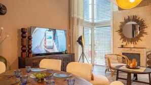 Uma área de refeições com uma mesa redonda posta para quatro pessoas, uma televisão em um móvel e uma lareira.