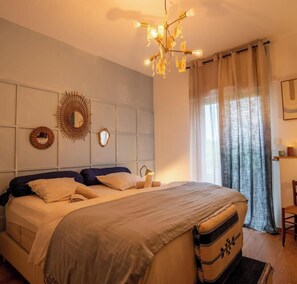 Ein Schlafzimmer mit einem Bett, einer Chandelüster, einem Spiegel und einem Fenster mit Vorhängen.