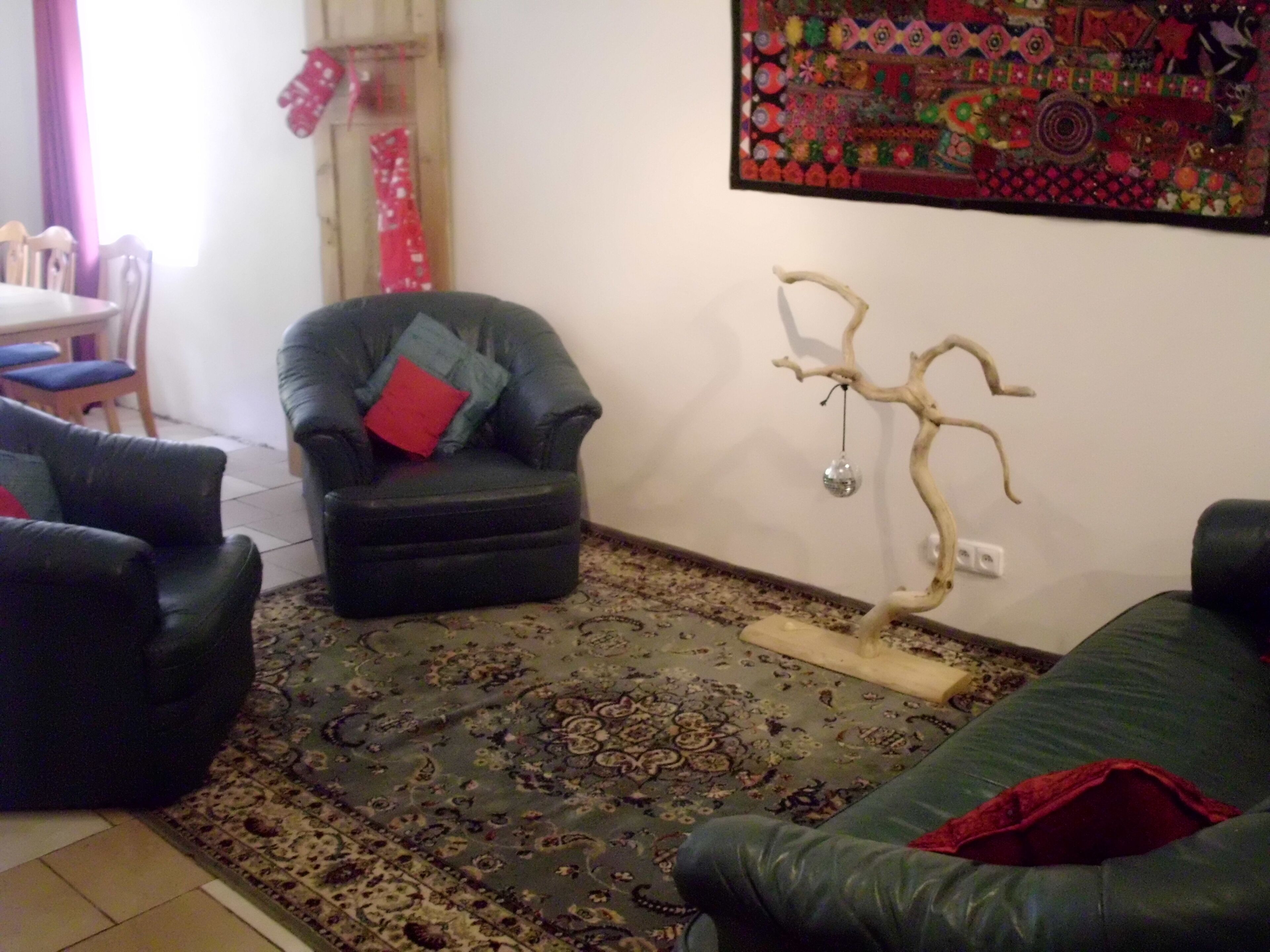 Een woonkamer met een zwarte leren bank, een zwarte fauteuil met rode en blauwe kussens, een kamerbreed tapijt en een decoratief object aan de muur.