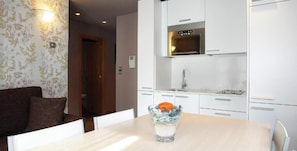 A modern kitchen with white cabinets, a stainless steel microwave, and a glass table with a salt shaker.