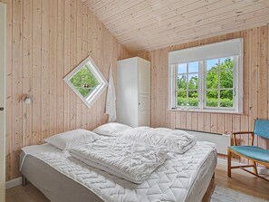 Ein Schlafzimmer mit Bett, Fenster, Stuhl und Holzwänden.