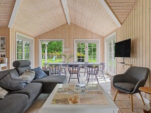 Ein geräumiges Wohnzimmer mit hohen Decken, Holzwänden, einem Essbereich und einem Fernseher.