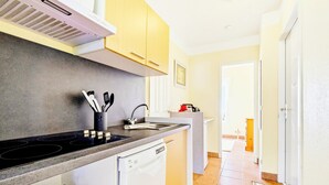 Una cucina con forno, lavello e lavastoviglie, un corridoio con una porta e un pavimento piastrellato.