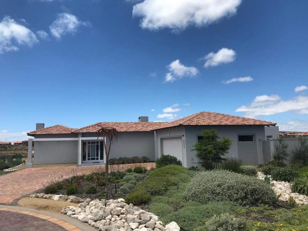A two-story house with a tiled roof, a garage, and a landscaped garden with various plants and a rock feature.