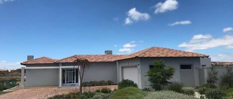 A two-story house with a tiled roof, a garage, and a landscaped garden with various plants and a rock feature.