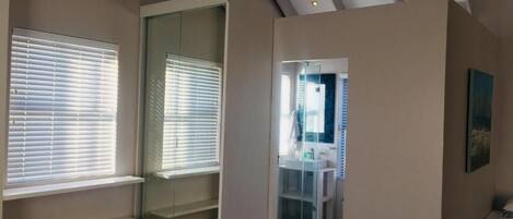 A room with a glass shower enclosure, a bed, and a view of the bathroom.
