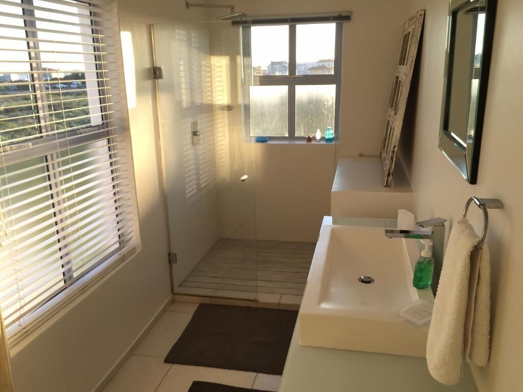 Een badkamer met een douche, een wastafel, een raam en een handdoekhouder.