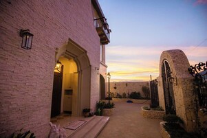 Um edifício de tijolos com uma entrada em arco, um portão de pedra e vista para o pôr do sol.