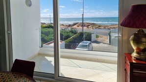 Et værelse med en stor skydedør, der fører ud til en balkon med udsigt over stranden og havet.
