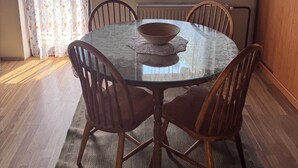 Un coin repas avec une table ronde en verre, des chaises en bois, un saladier et des rideaux à motifs floraux.