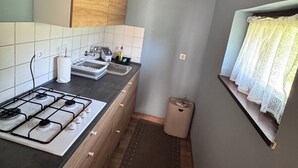 Une cuisine équipée d’une cuisinière à gaz, de meubles en bois, d’un plan de travail carrelé et d’une fenêtre ornée de rideaux en dentelle.