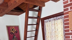 Une pièce avec une échelle en bois, un radiateur blanc, un rideau à motifs floraux et un tableau encadré accroché au mur.