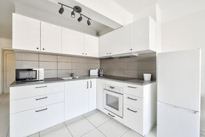 Een moderne keuken met witte kastjes, een magnetron, een broodrooster en een koelkast.