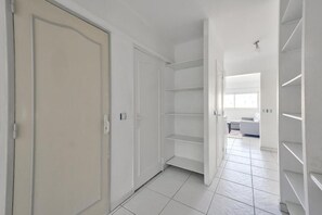 Een gang met witte deuren en planken, die leidt naar een kamer met een witte bank en een raam.