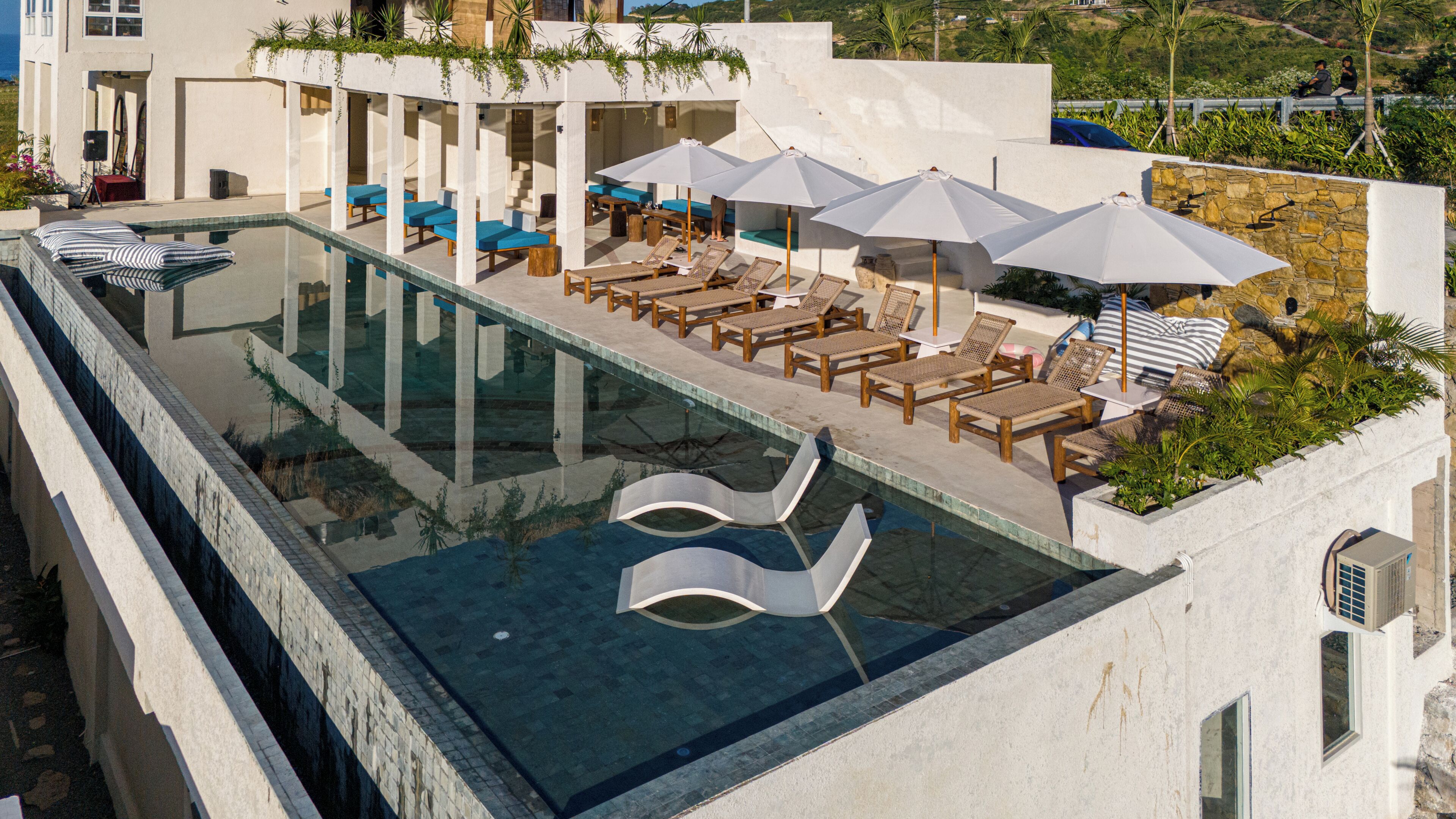A rooftop infinity pool with lounge chairs and umbrellas, surrounded by a white building with stone accents.