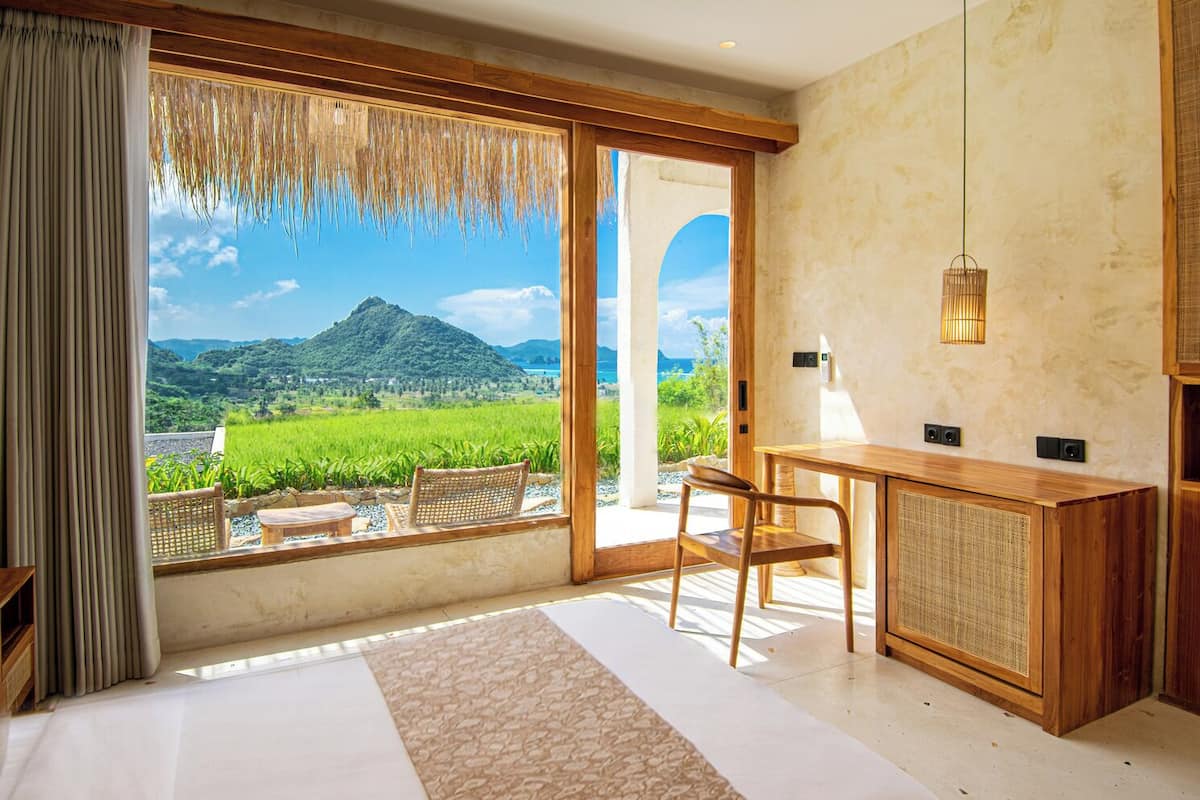 Une pièce dotée d’une grande fenêtre, d’un bureau en bois, d’une chaise et offrant une vue sur un paysage verdoyant avec des montagnes.