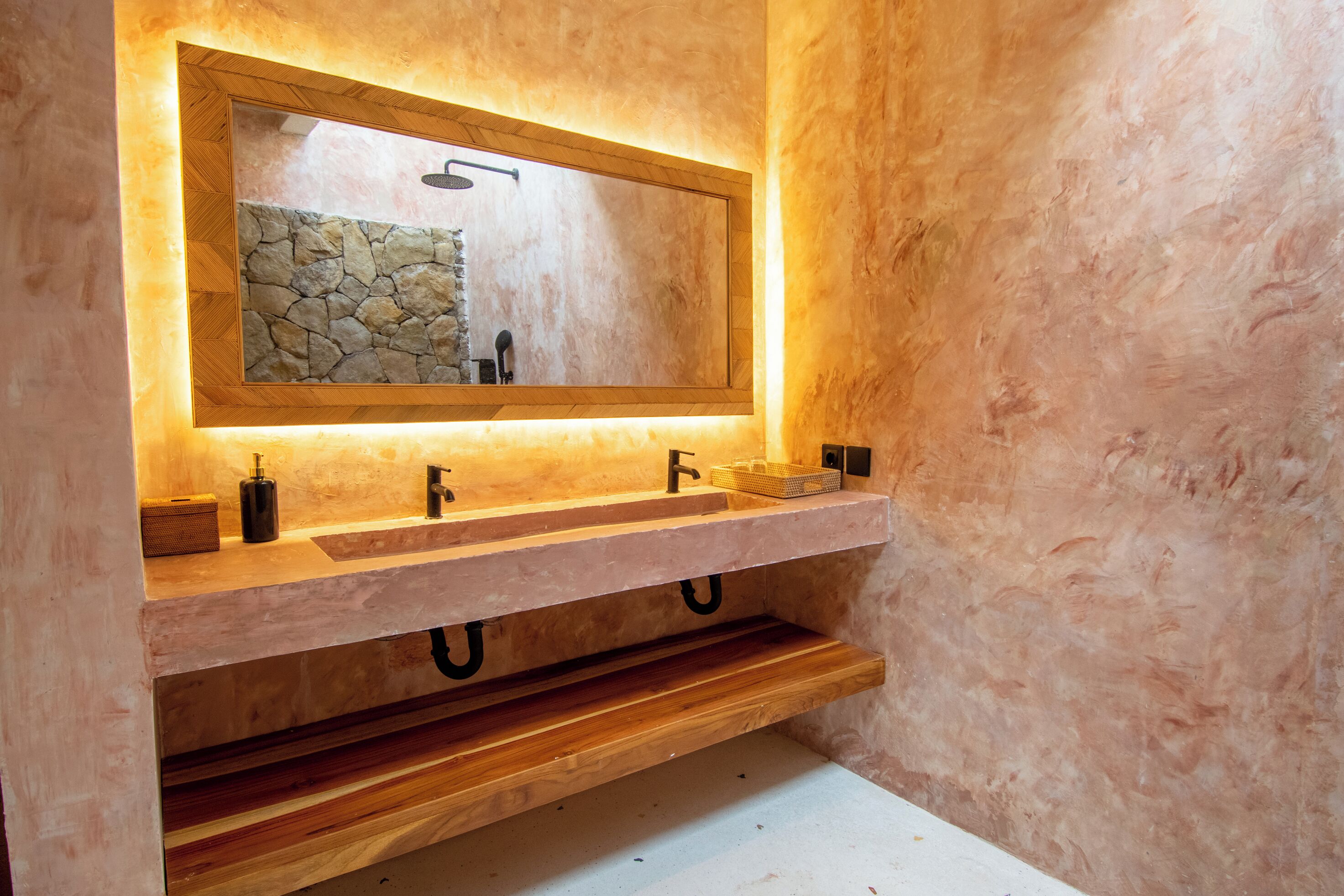 A bathroom with a wooden vanity, a stone backsplash, and a mirror with a wooden frame.