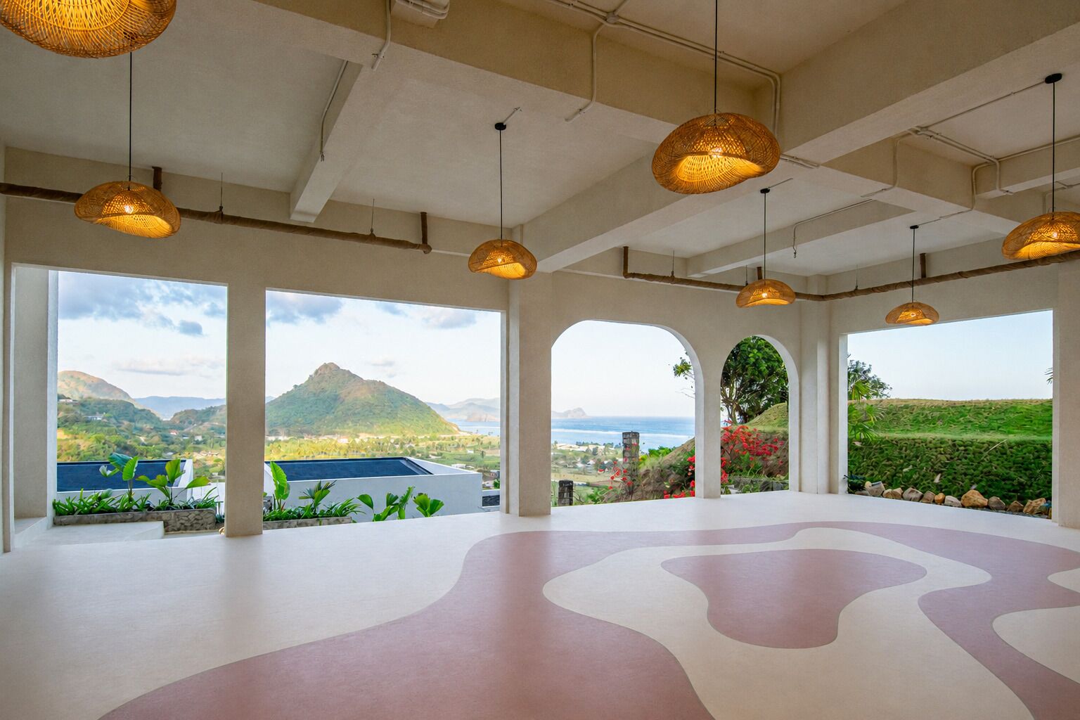 Amplia habitación con ventanas grandes, diseño de piso curvo y lámparas colgantes de mimbre.