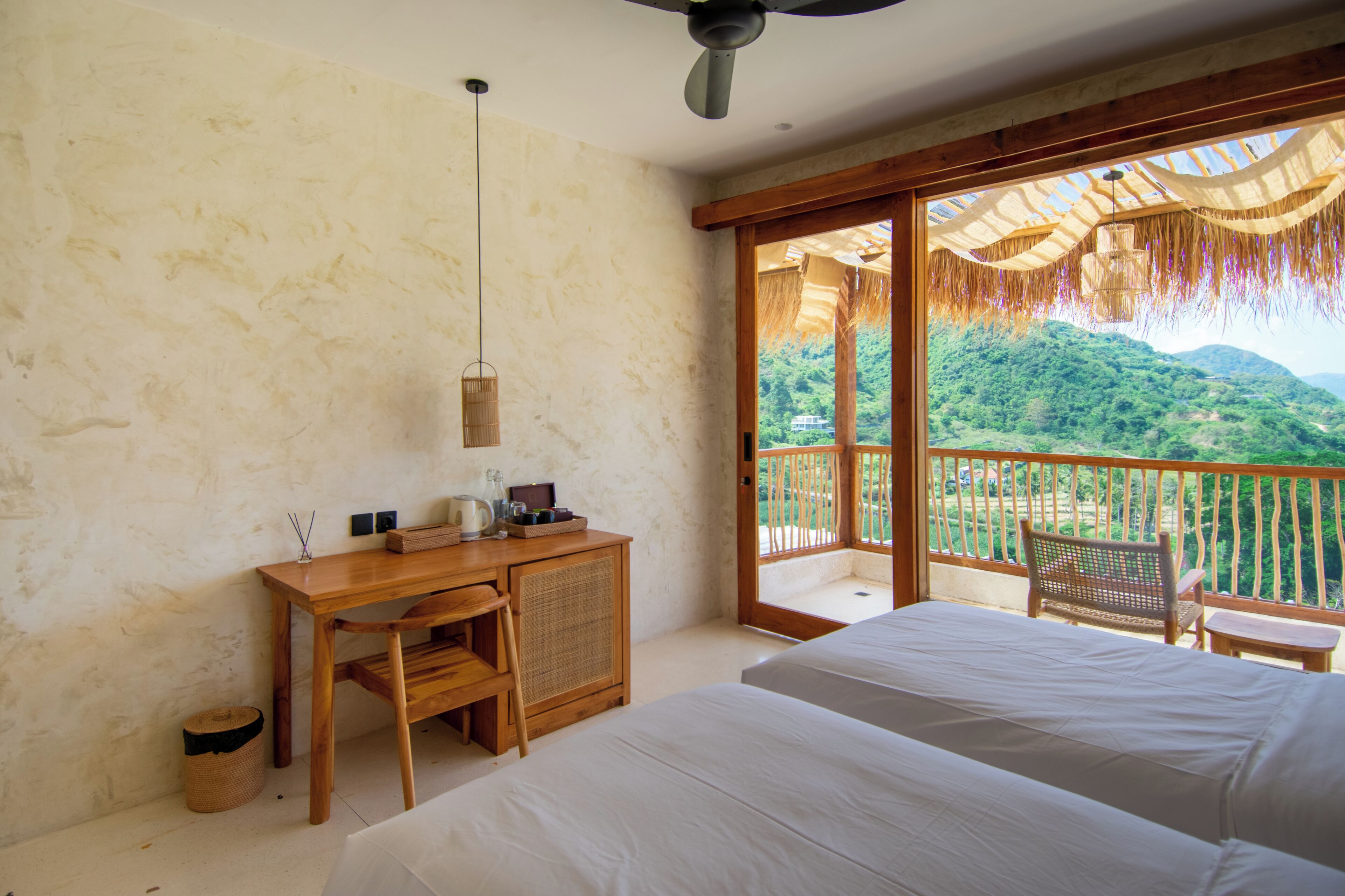 Un dormitorio con una cama grande, un escritorio de madera y vistas a un paisaje exuberante a través de una puerta corredera de vidrio.