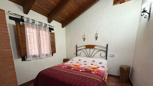A bedroom with a bed, a window with curtains, a wooden ceiling, and a wall-mounted light fixture.