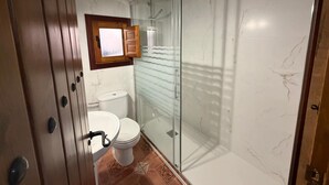 A bathroom with a toilet, a shower with glass doors, and a window above the toilet.