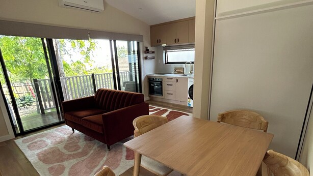 A modern kitchen with a dining area, a sofa, and a view of the outdoors.