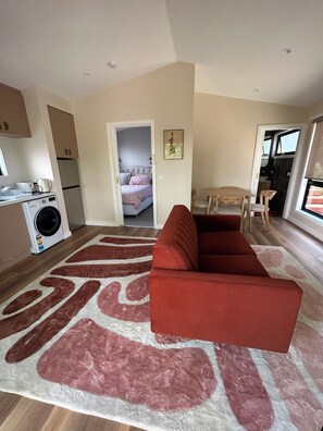 Een knus woongedeelte met een bank, een eethoek, een keuken met een wasmachine en een slaapkamer met een bed.