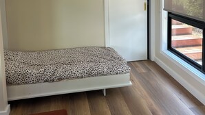 A room with a bed, a window, a door, and a small bench.