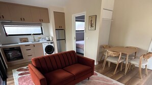 A compact living space with a sofa, a dining table with chairs, a kitchen area with appliances, and a small bedroom visible through an open door.