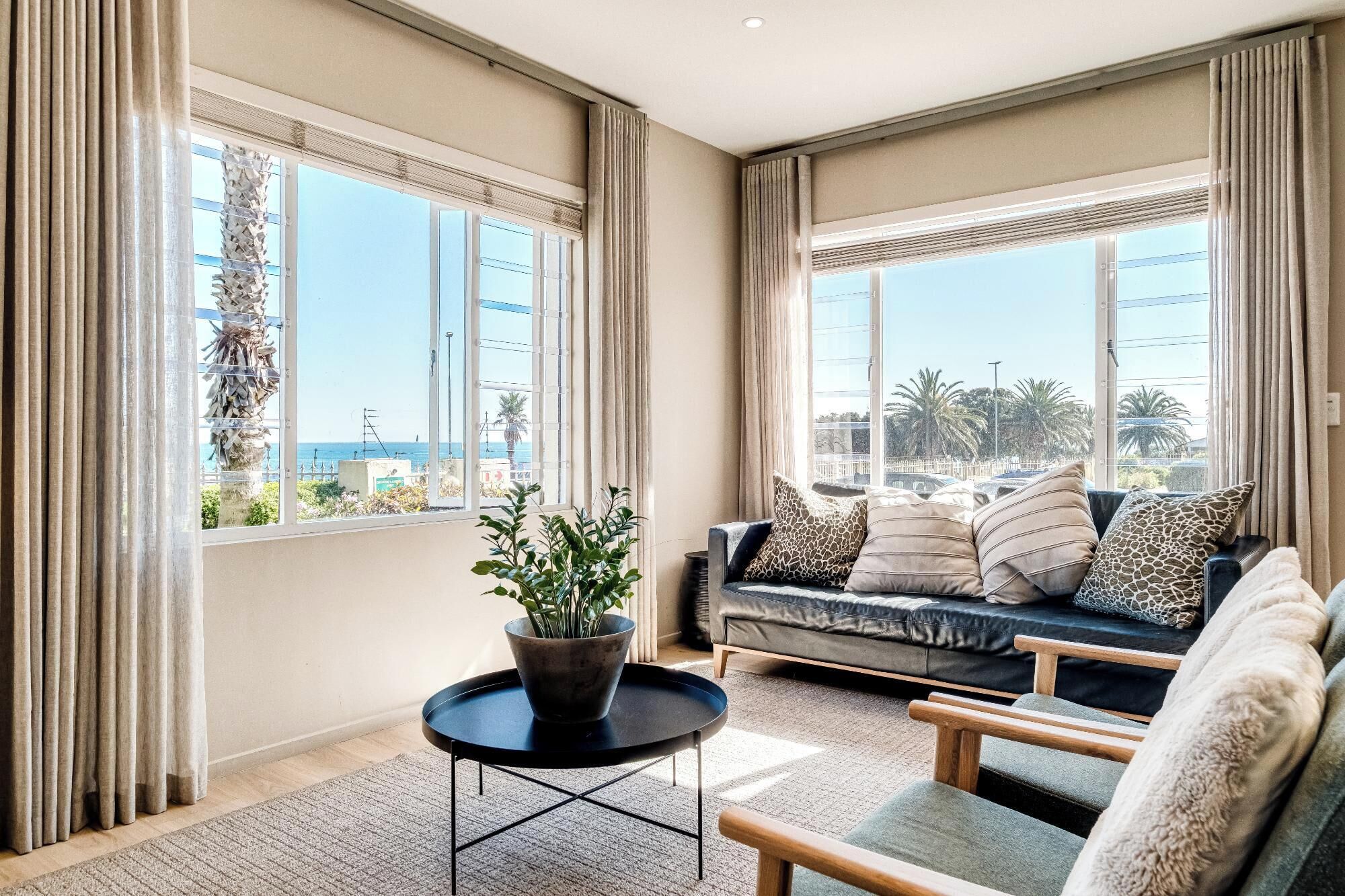 A modern living room with a sofa, armchairs, a coffee table, and a potted plant.