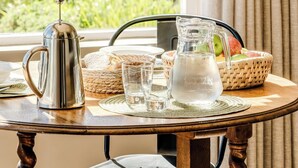 Una mesa con una cafetera, vasos, una jarra y una cesta de frutas.