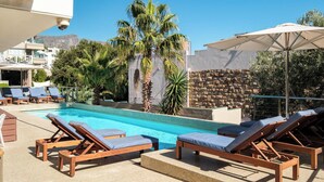 Zona de piscina con sillones reclinables, una pared de piedra y palmeras.