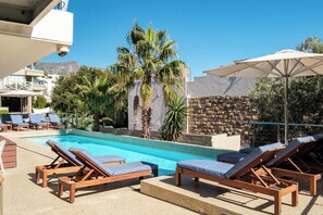 Zona de piscina con sillones reclinables, una pared de piedra y palmeras.