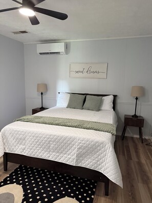 Ein Schlafzimmer mit einem Bett, zwei Nachttischen, einem Deckenventilator, einer Klimaanlage und einem an der Wand befestigten Schild.