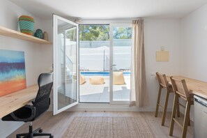 A modern kitchen with a dining area, a glass door leading to a pool, and a painting on the wall.